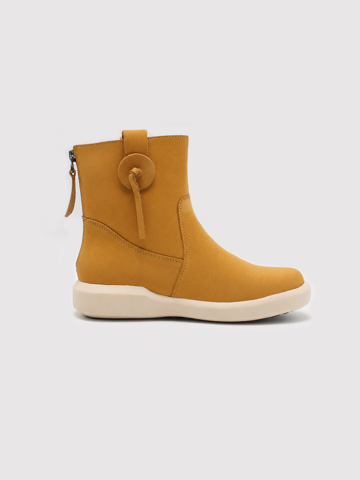 Side profile of a yellow suede ankle boot with a decorative loop detail, rear zipper and cream sole.