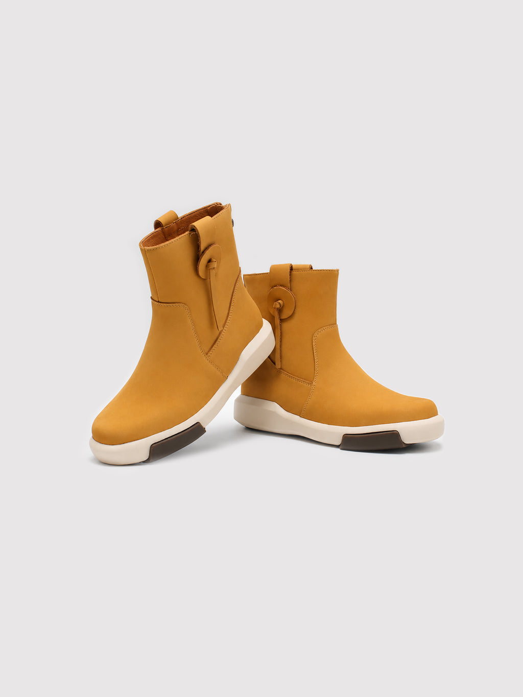 Yellow suede ankle boots arranged with one boot tilted, showing the rounded toes and contrasting cream soles.