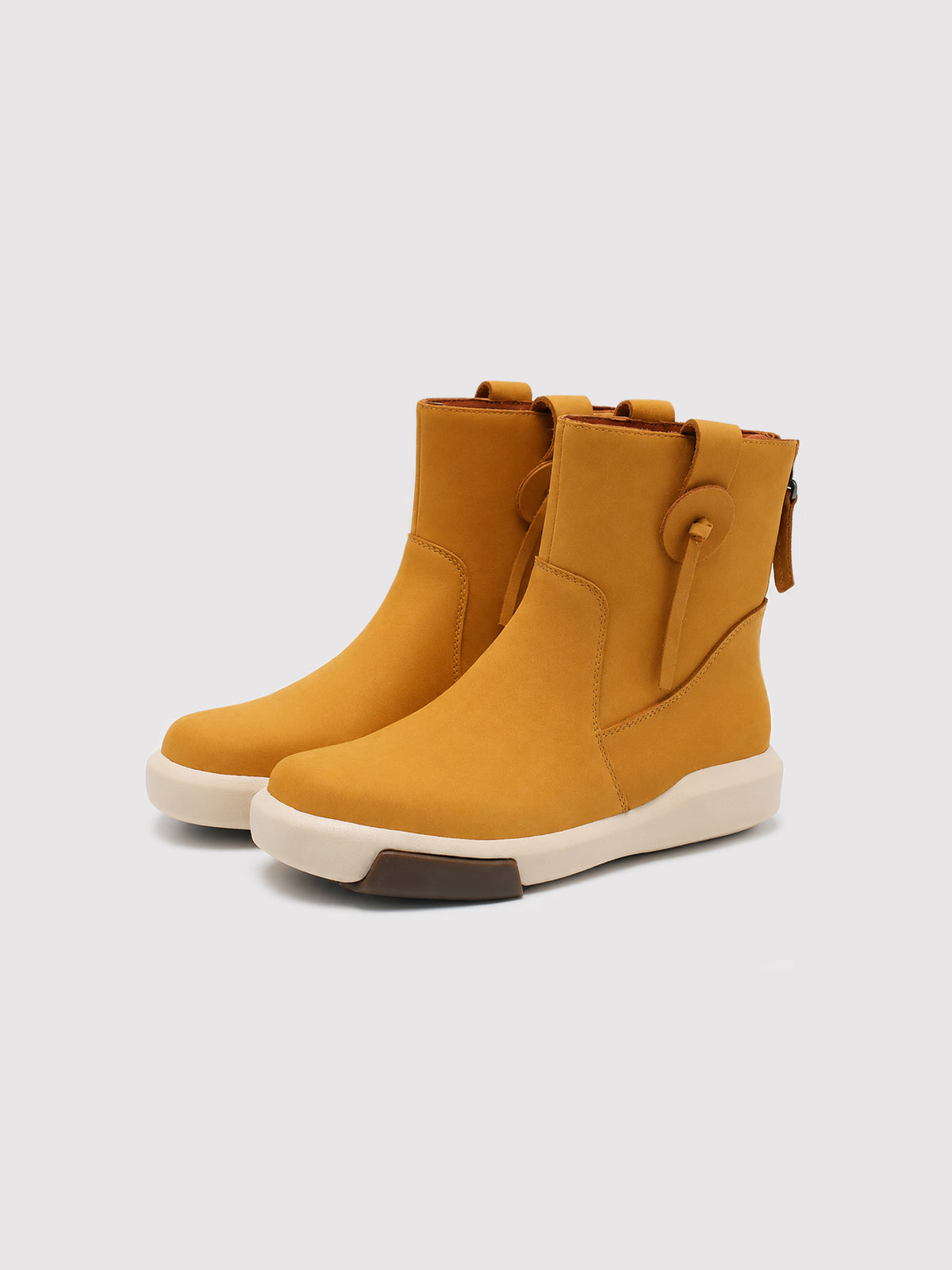 Pair of mustard-yellow suede ankle boots with decorative side loops and cream soles, shown from a front three-quarter angle.