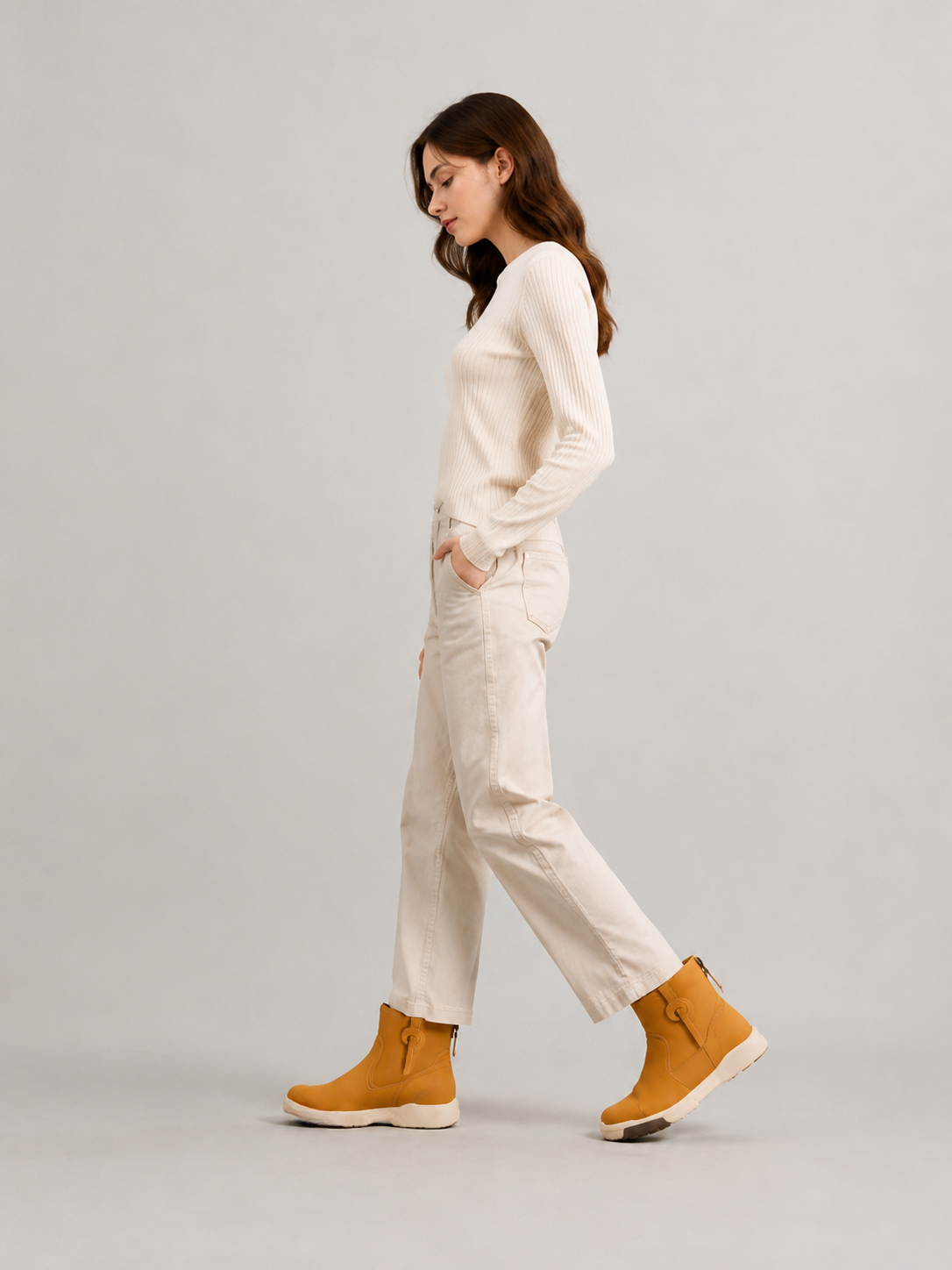 Side view of a model walking in yellow suede ankle boots with cropped ivory trousers and a cream sweater.