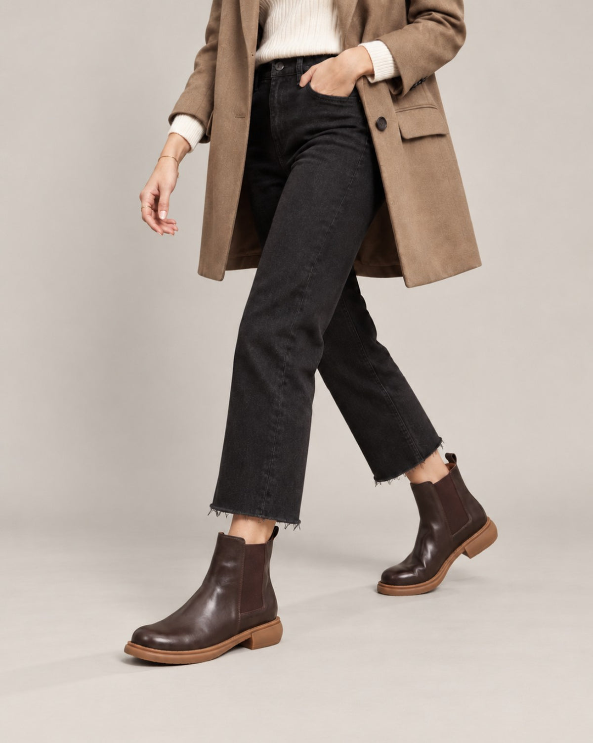 On-foot view of brown leather Chelsea boots styled with cropped black jeans and a brown blazer.