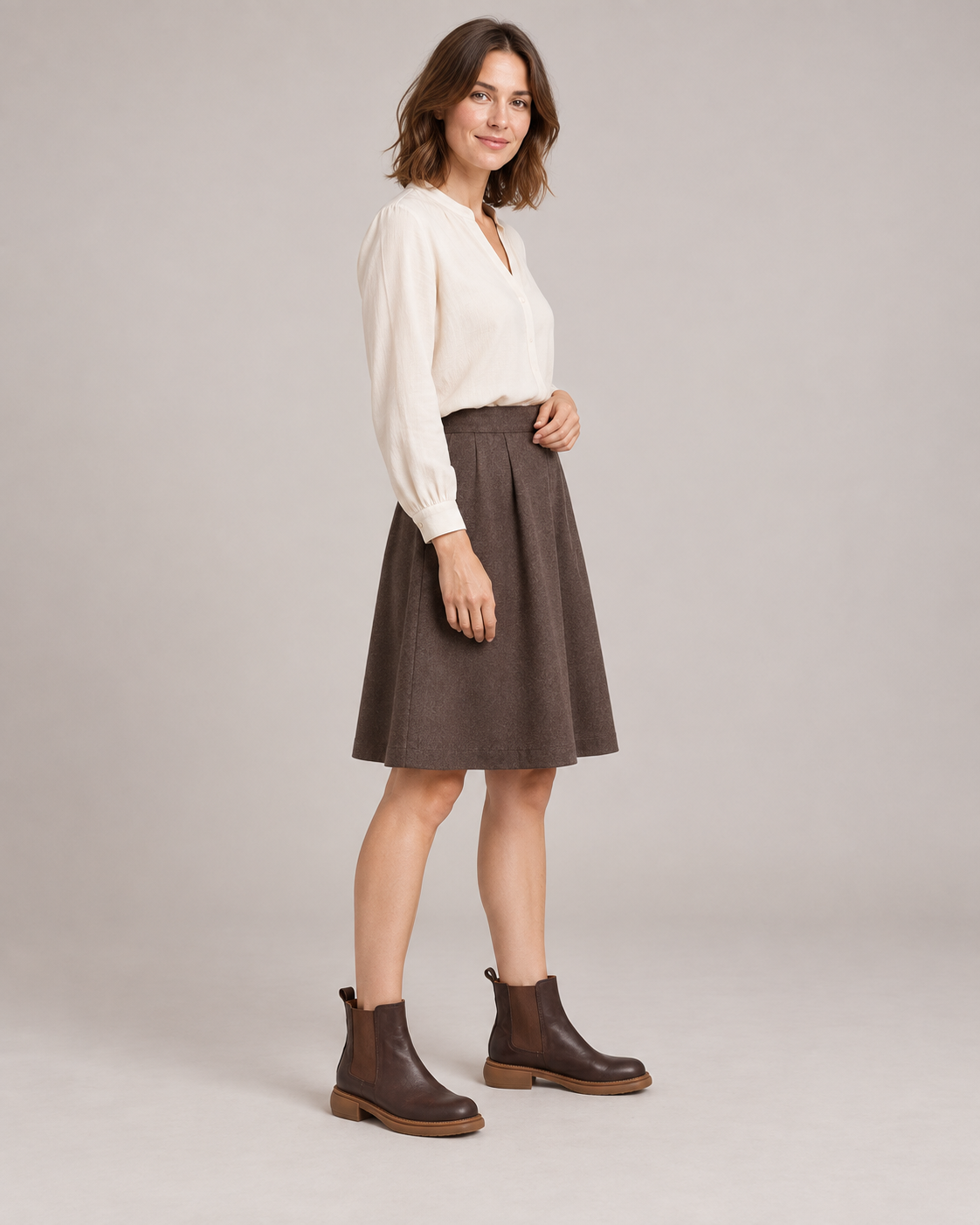 Standing model wearing brown leather Chelsea boots with a white blouse and a brown knee-length skirt.